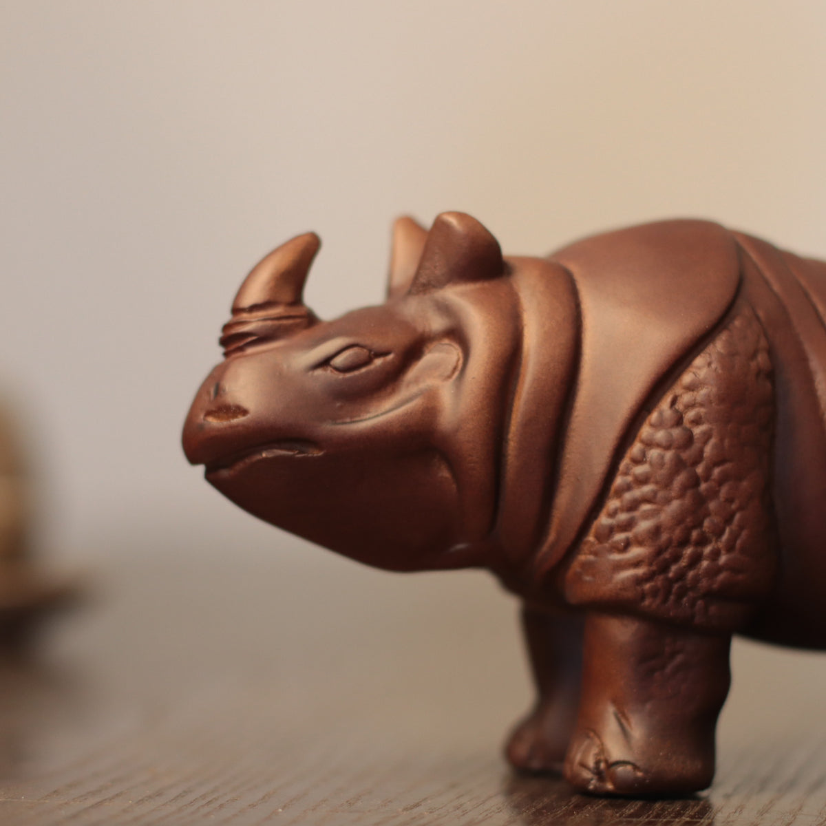 A close-up of a brown wooden rhinoceros figurine standing on a wooden surface against a soft beige background.