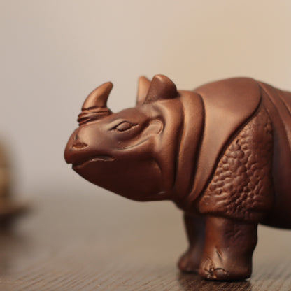 A close-up of a brown wooden rhinoceros figurine standing on a wooden surface against a soft beige background.