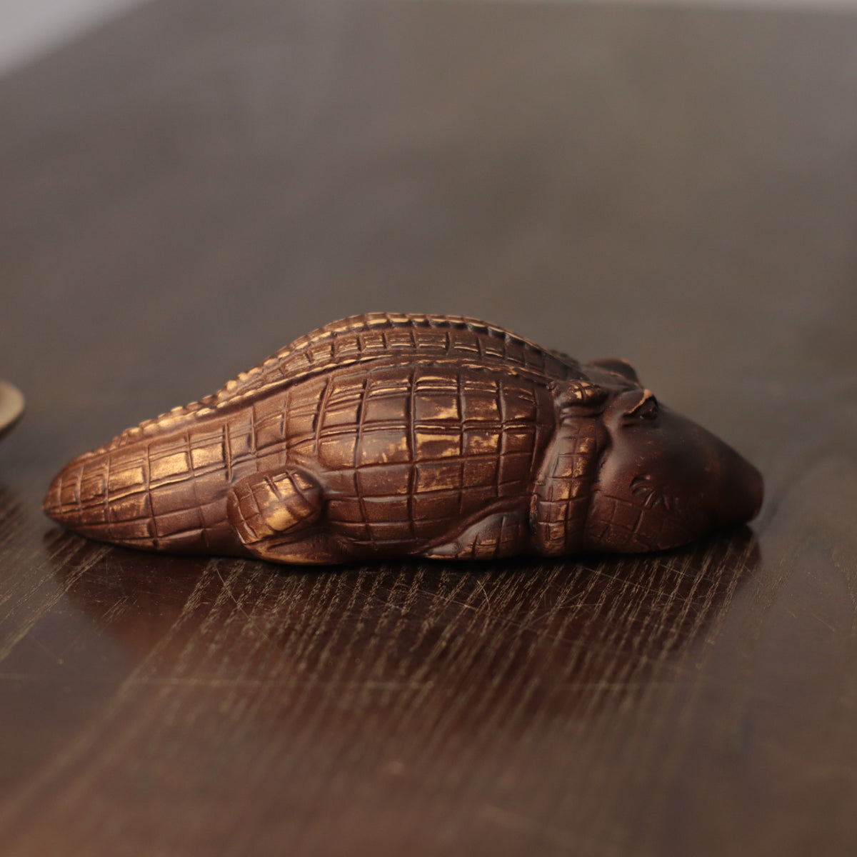 A small carved alligator figurine in a dark metallic bronze finish, resting on a dark wooden surface.