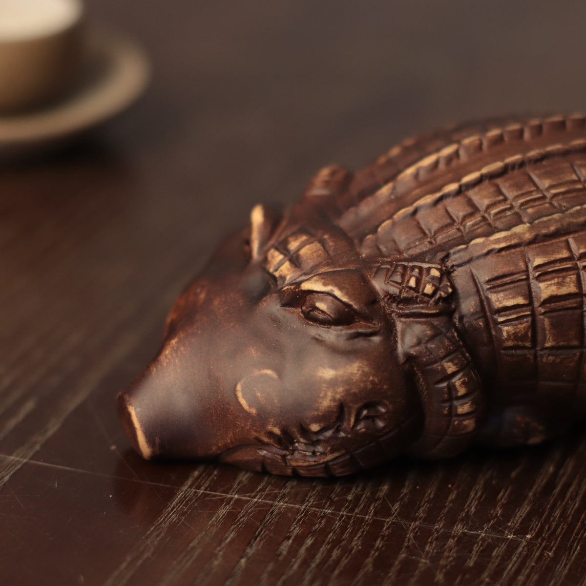 A close-up of a dark bronze decorative object shaped like a crocodile or alligator head, resting on a dark wooden surface.